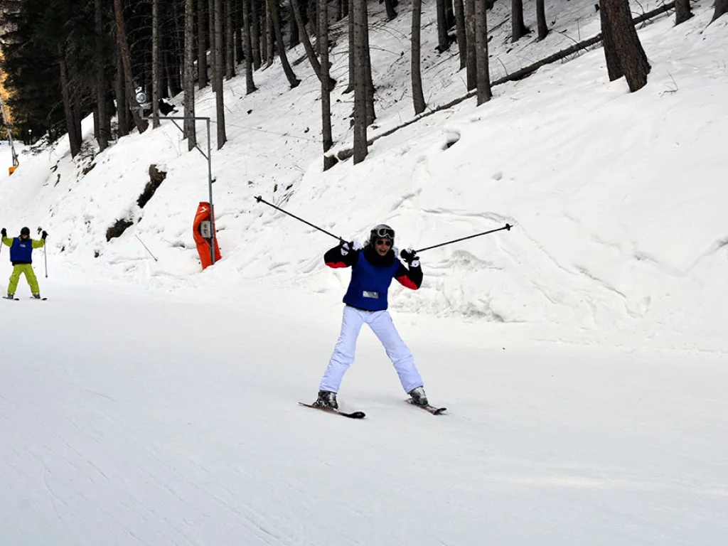 Skifahrerin in weißer Hose am Hang unterhalb des Waldes.